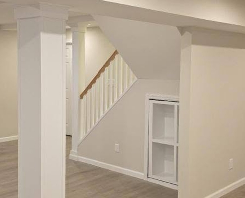 Finished basement in Suffolk County with white wrapped support columns, open staircase, built-in shelving and gray vinyl plank flooring