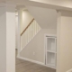 Finished basement in Suffolk County with white wrapped support columns, open staircase, built-in shelving and gray vinyl plank flooring