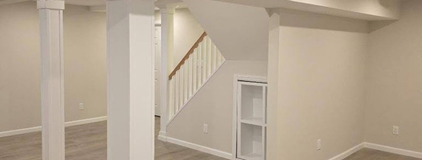 Finished basement in Suffolk County with white wrapped support columns, open staircase, built-in shelving and gray vinyl plank flooring