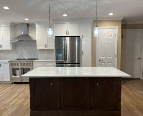 Modern renovated kitchen featuring a dark wood island with white marble countertop, stainless steel appliances, and white cabinetry in a Suffolk County home addition.