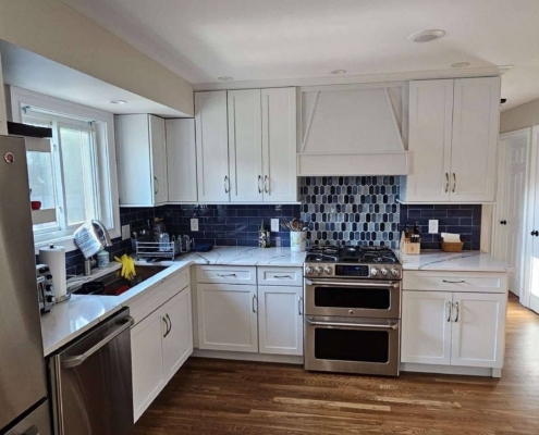 Remodeled kitchen featuring white shaker cabinets, dark blue tile backsplash, stainless steel appliances, and white marble-look counter.