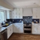 Remodeled kitchen featuring white shaker cabinets, dark blue tile backsplash, stainless steel appliances, and white marble-look counter.