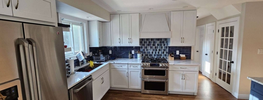Remodeled kitchen featuring white shaker cabinets, dark blue tile backsplash, stainless steel appliances, and white marble-look counter.