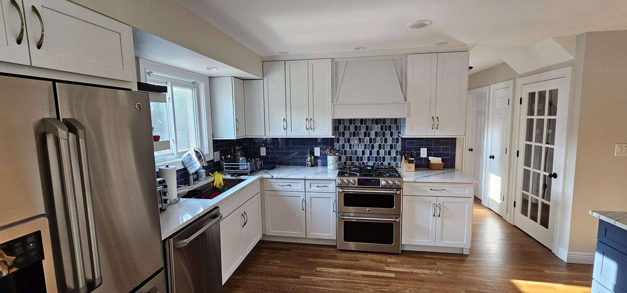 Remodeled kitchen featuring white shaker cabinets, dark blue tile backsplash, stainless steel appliances, and white marble-look counter.