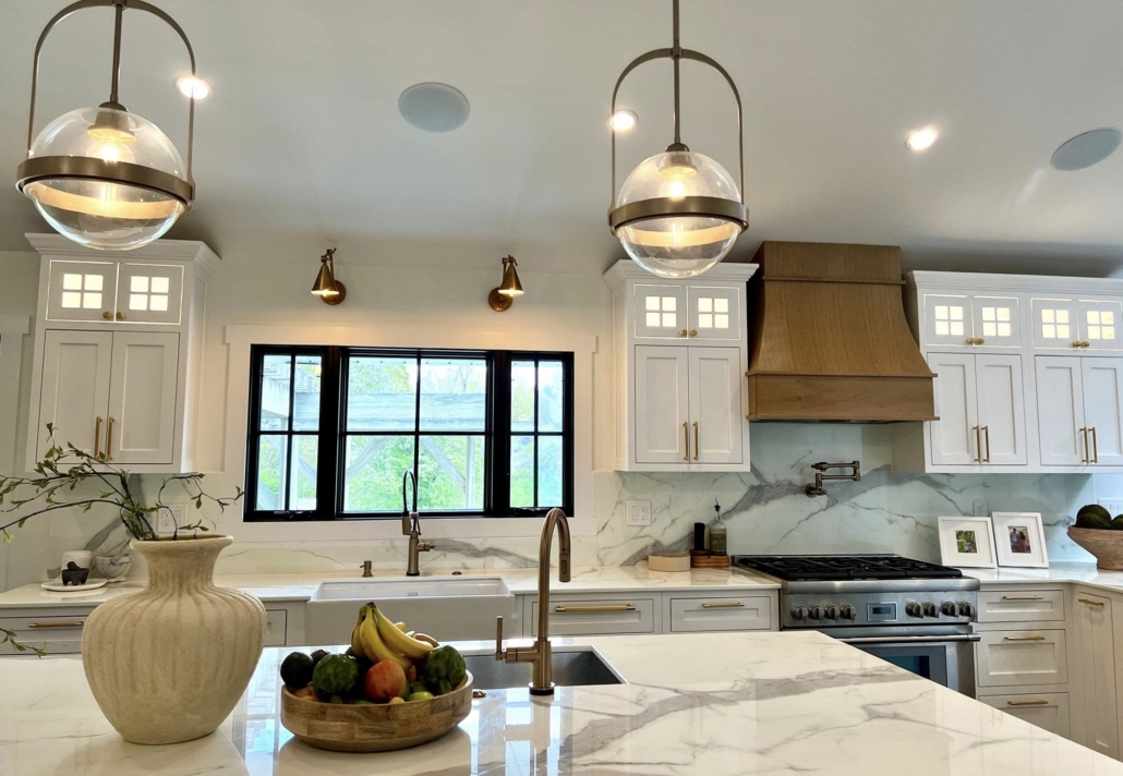 Remodeled kitchen in Suffolk County with white shaker cabinets, brass hardware, wood range hood and marble-look slab backsplash